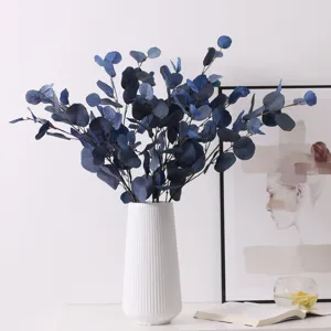 Detailed view of artificial blue eucalyptus branches in a white ceramic vase for home decor.