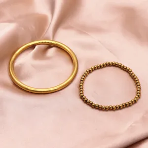 Close-up of golden brass matte bangle and beaded bracelet set on pink satin fabric.