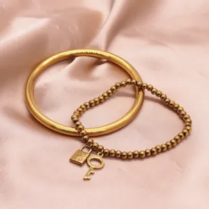 Gold-plated brass bangle and beaded charm bracelet set with lock and key pendants for women.