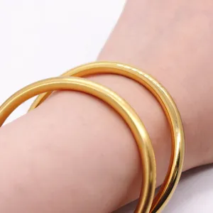 Close-up detail of solid matte gold-plated bangles worn on wrist, showing fine frosted texture.