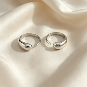 Gros plan de detail des bagues ouvertes en argent poli sur fond de tissu en soie douce.
