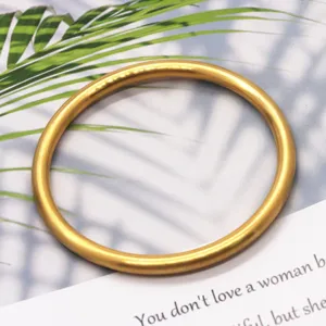 Closeup shot of a solid matte gold brass bangle, showing fine texture and smooth curve.