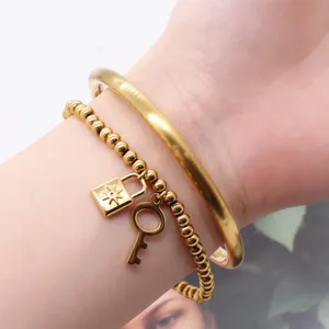 Close-up detail shot of stackable gold-plated bangle and beaded charm bracelet with lock.