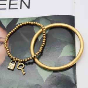 Detailed shot of gold-plated beaded bracelet with lock key pendant and solid plain bangle.