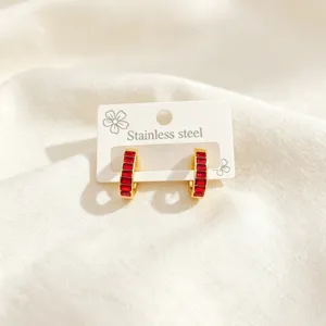 Detail shot of gold U-shaped hoop earrings with red baguette stones and stainless steel mark.