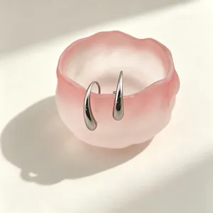 Close-up of elegant metallic teardrop earrings displayed in a pink frosted bowl on table.