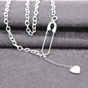 Close-up detail of the silver safety pin necklace with heart charm on textured background.
