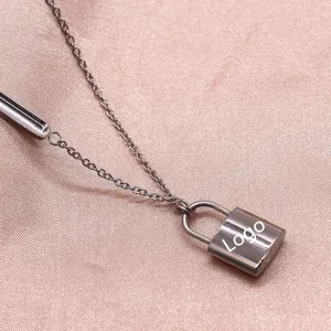Close-up detail of silver tone metal necklace featuring an engraved lock pendant and side bar.