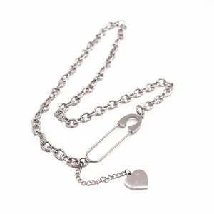 Close-up view of the silver safety pin necklace with heart pendant, metallic texture detail.