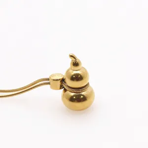 Detail shot of a gold gourd pendant necklace with a fine snake chain and metal loop.
