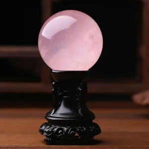 Detailed view of natural rose quartz crystal sphere on carved stand, elegant home decor accent.