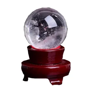 Natural clear quartz crystal ball with dark red wooden base for home decor feng shui display.