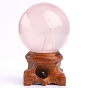 Natural rose quartz crystal sphere with wooden base for home decor and healing energy display.