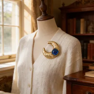 Detailopname van vintage gouden maan broche met blauwe harssteen op gebreid vestje.