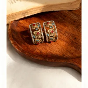 Nahaufnahme von vintage goldenen Rosenrelief Ohrringen mit roten und blauen Strasssteinen.