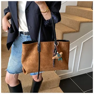 Detail view of a chic brown suede tote bag with diamond pattern and a cute bear keychain charm.