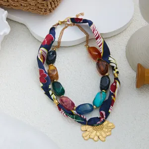 Detalle de collar de bufanda de seda floral multicapa con cuentas acrílicas y colgante de oro.