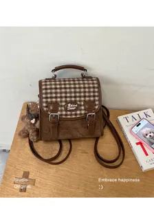 Vue détaillée du mini sac à dos rétro à carreaux marron avec finitions en cuir et pendentif.