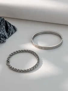 Stainless steel Roman numeral bangle and chain bracelet detail shot, silver metal texture.