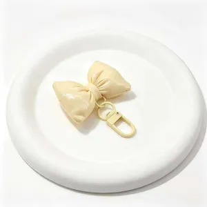 Nahaufnahme eines niedlichen beigen Leder-Schleifen-Schlüsselanhängers mit goldenen Beschlägen.