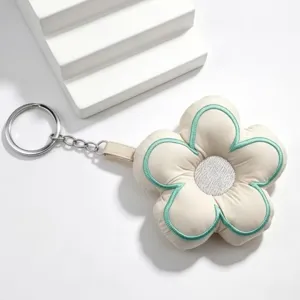 Close-up detail of cute embroidered five-petal flower keychain pendant in beige and green fabric.