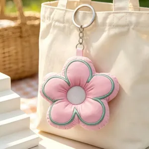 Close up detail shot of a cute pink padded floral keychain hanging on a white tote bag.
