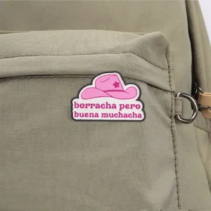 Grüner Rucksack Detailansicht mit einem rosa Cowboyhut-Abzeichen und spanischem Text.