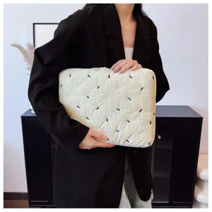 Detailed view of a quilted laptop sleeve with colorful embroidery stitches held by model.