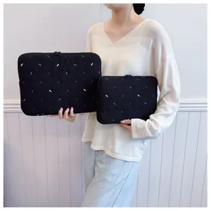 Black padded laptop sleeve detail showing colorful embroidered stitches and smooth zipper closure.