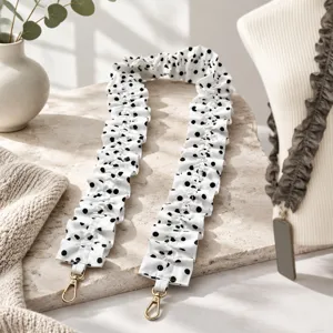 Detailed view of white and black polka dot ruffled scrunchie bag strap, textured prop scene.