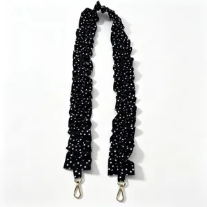 Detailed view of the black and white polka dot pleated strap with gold metal clasps.