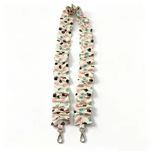 Detailed view of elastic ruffled bag strap with cute paw print pattern and gold metal clasps.