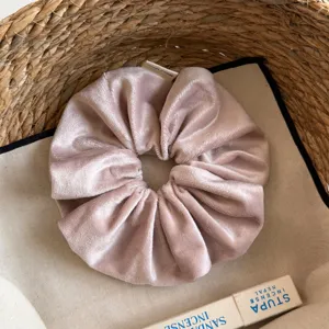 Gedetailleerd overzicht van een zachte roze fluwelen haarscrunchie met een klein label.