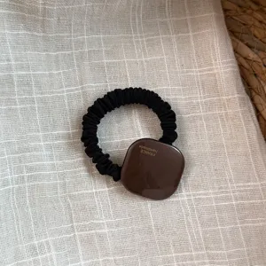 Primer plano detallado de una goma de pelo elástica negra con adorno cuadrado de acetato.