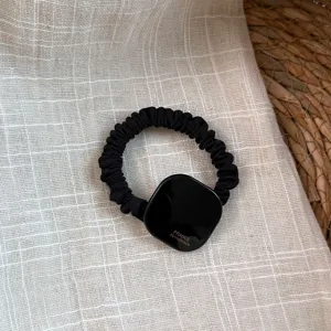 Primer plano detallado de una goma para el pelo negra con una placa cuadrada lisa y elegante.