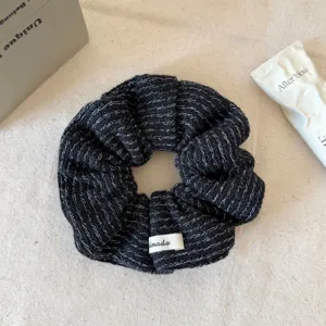 Close-up van een stijlvolle zwarte gebreide haarscrunchie met witte textuur en label.