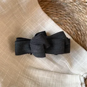 Gros plan détail d'une pince à cheveux nœud en tissu texturé gris foncé sur tissu.