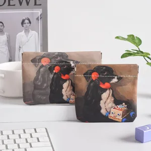 Detail view of mini leather self-closing coin purse with vintage black dog illustration on clean desk.