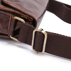 Close-up detail of brown vintage leather messenger bag strap and metal hardware buckle.