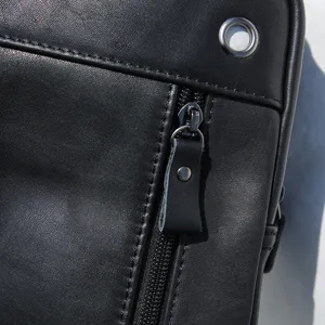 Primer plano detalle del bolso de pecho de cuero negro con costuras y cremallera.