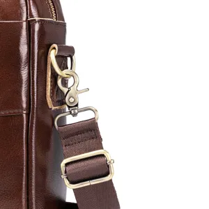 Detail shot of brown leather messenger bag shoulder strap hardware and metal clasp.