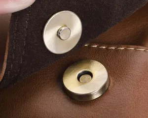 Close-up detail shot of the brown leather bag magnetic snap hardware and textured cowhide.