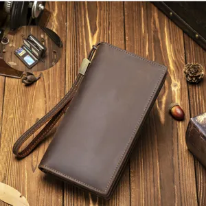 Close-up detail view of brown leather long wallet featuring wrist strap on rustic wood.