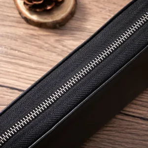 Black leather wallet zipper detail showing premium metallic texture and neat stitching.