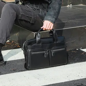 Men black leather briefcase detail view, showing texture, dual handles and front zipped pockets.