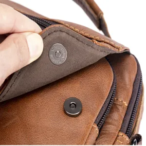 Close-up detail of men's leather bag metal magnetic snap button hardware craftsmanship.