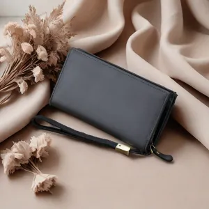 Detailed view of black genuine leather long wallet with wrist strap on beige fabric background.