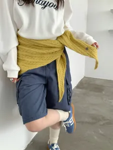 Nahaufnahme eines gelben Wollmischgewebe-Zopfstrick-Dreieckstuchs als schickes Wrap-Detail.