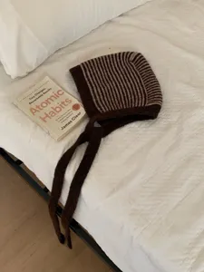 Detailed shot of a stylish brown striped knitted balaclava hat, warm winter ear protection scarf.