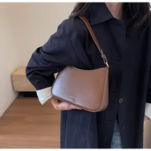 Brown leather baguette shoulder bag detail view, minimalist design with a metallic plaque.